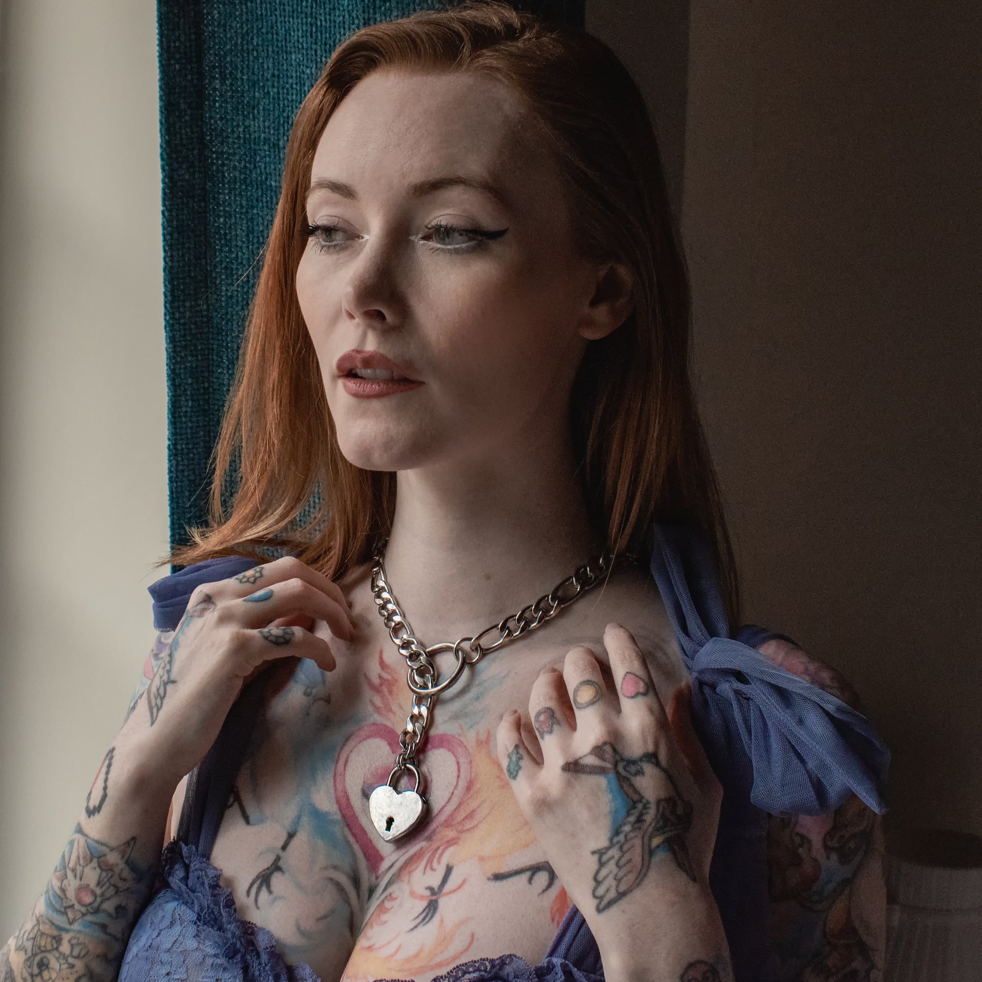 Beautiful model wears a silver coloured stainless steel slip chain necklace featuring a heart shapes padlock and large o ring