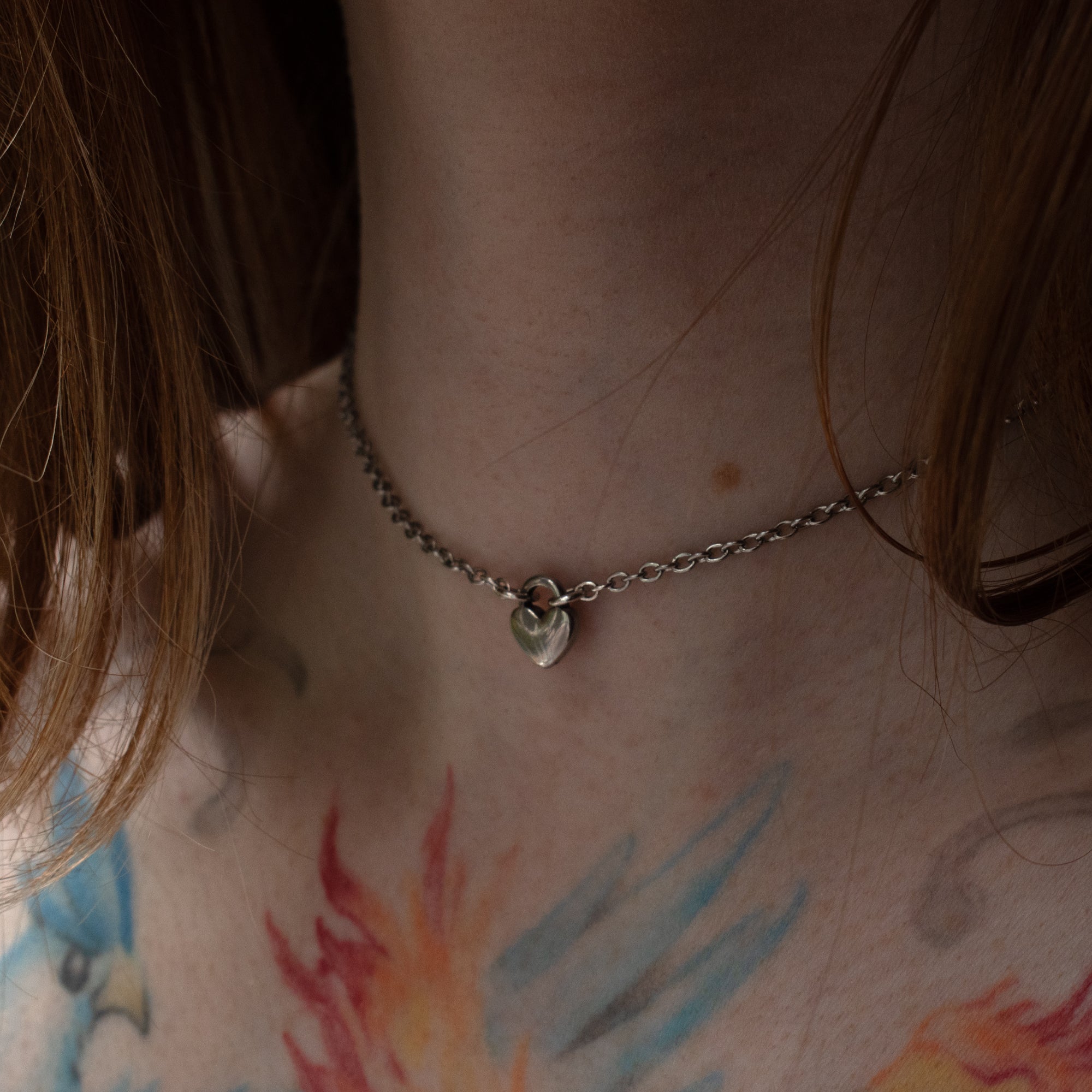 Tiny silver coloured heart pendant day collar on a dainty cable style chain, worn by model