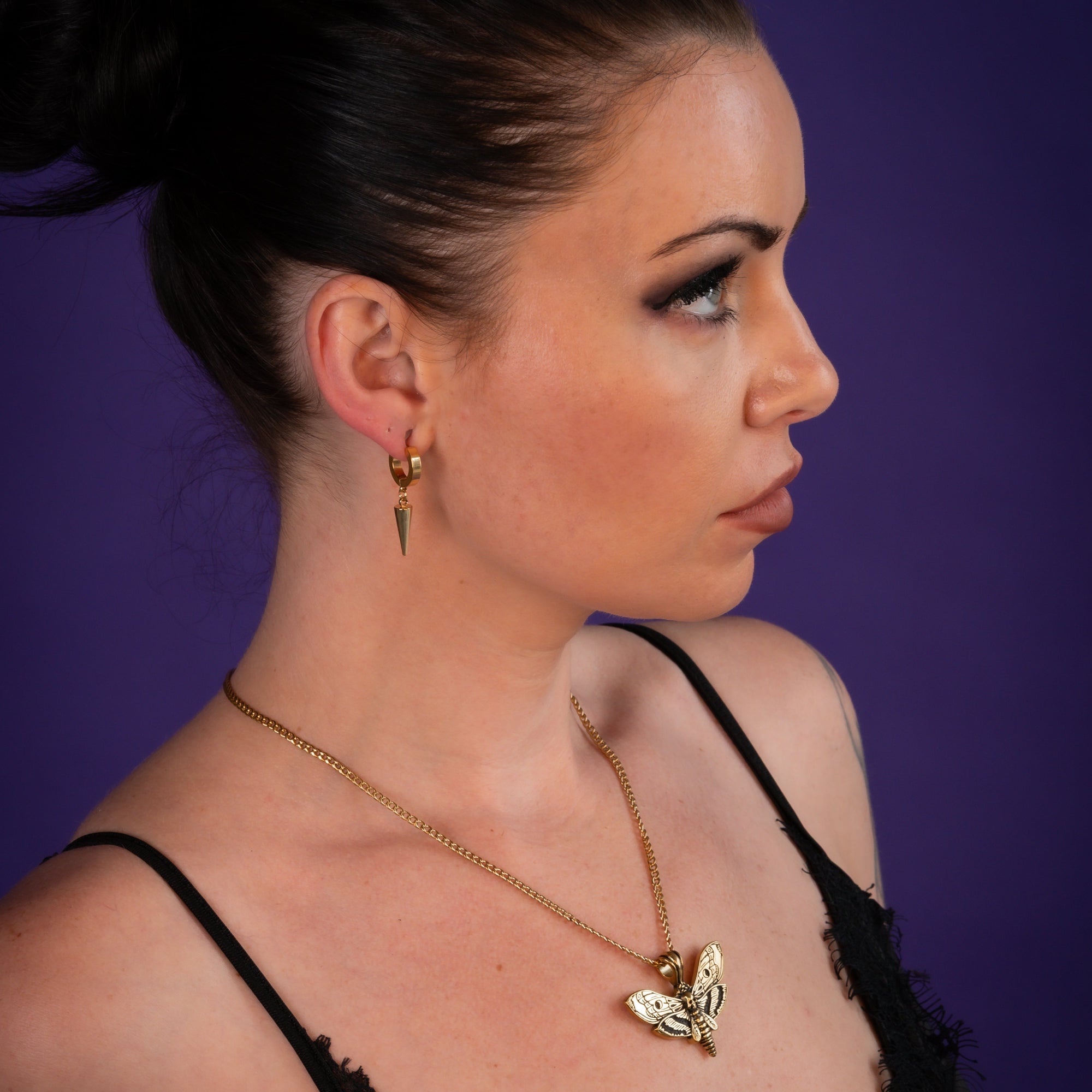 Woman wearing a gold death's head moth pendant on a dainty cuban chain necklace