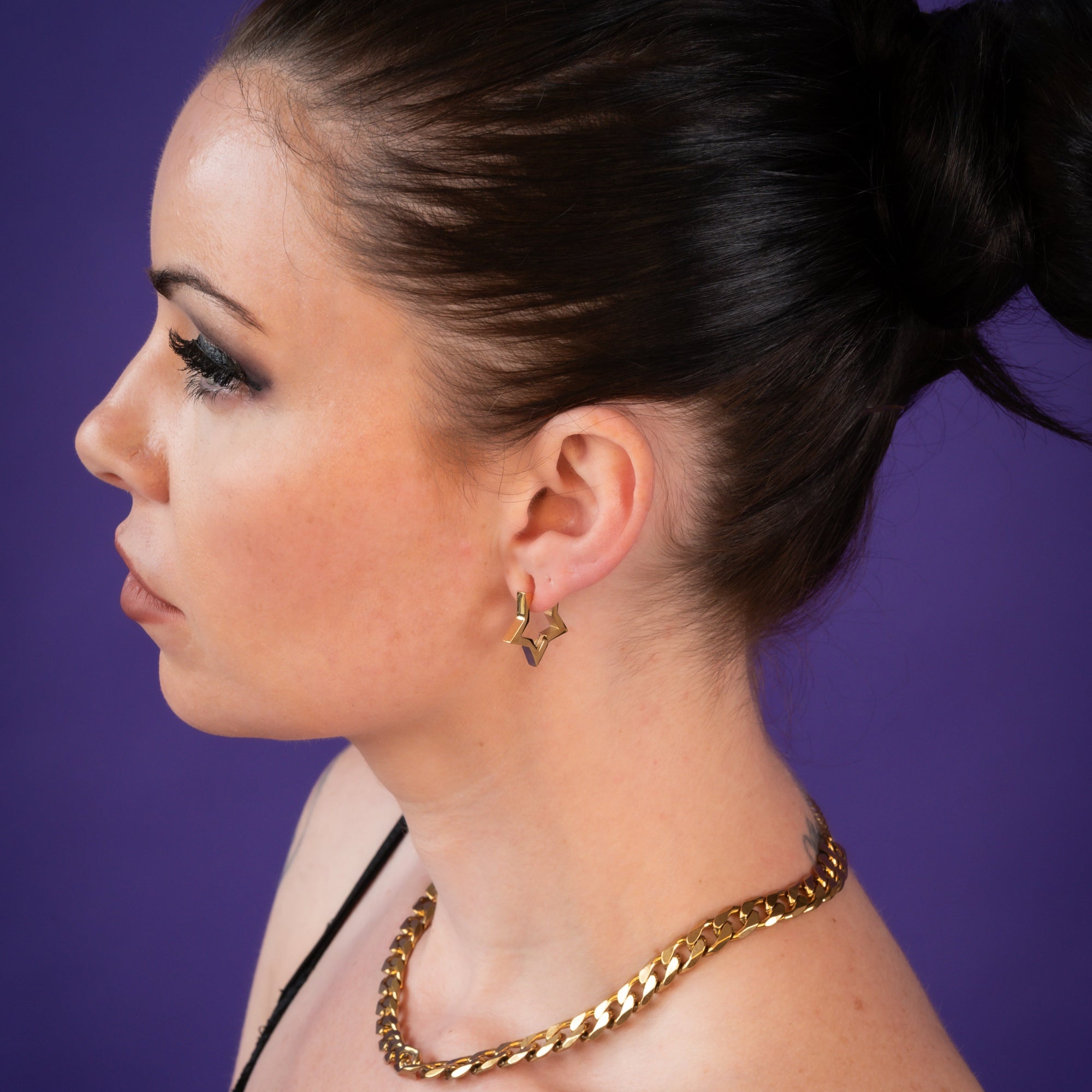Woman wears gold star huggie earrings with chunky gold cuabn choker