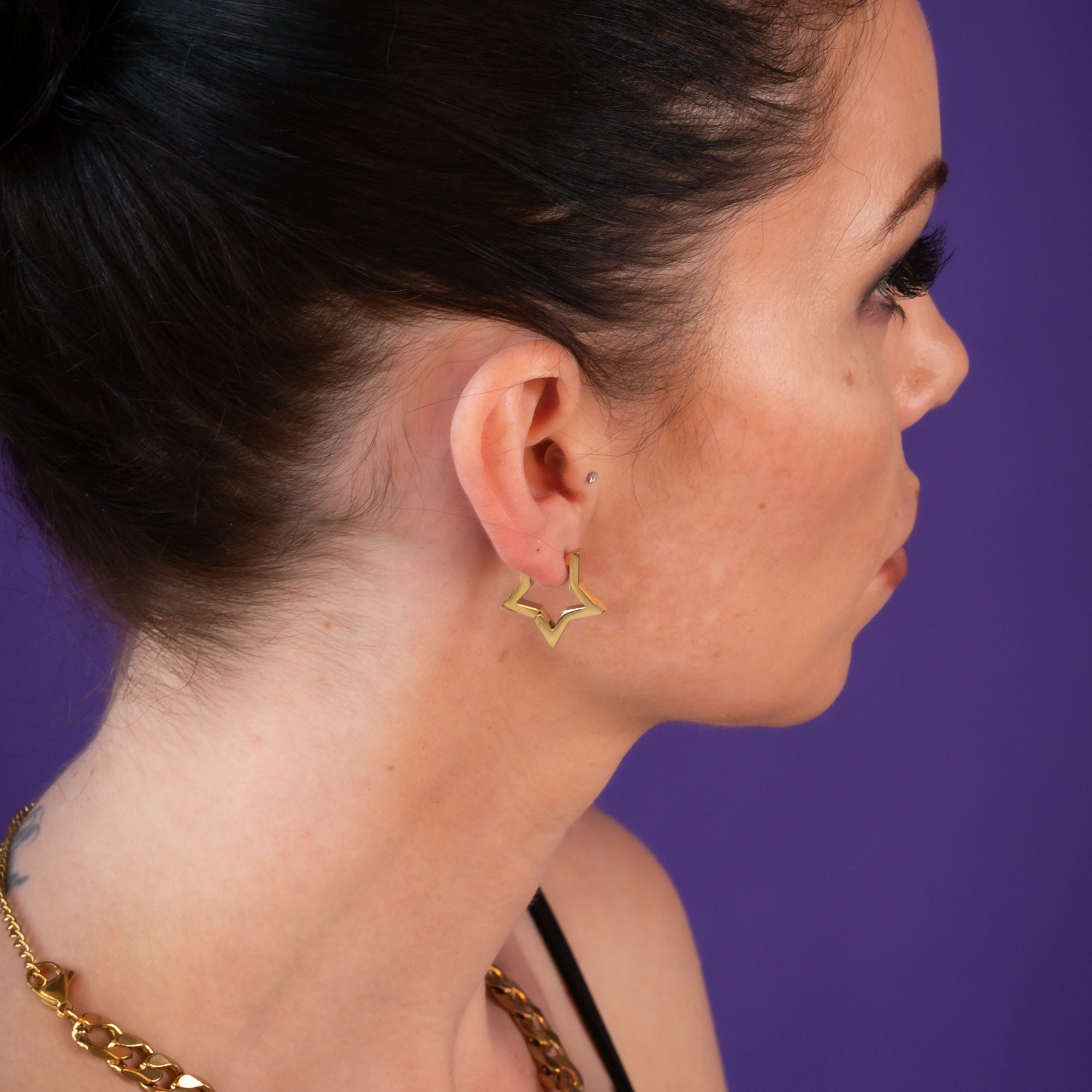 Woman wears gold star huggie earrings with chunky gold cuabn choker