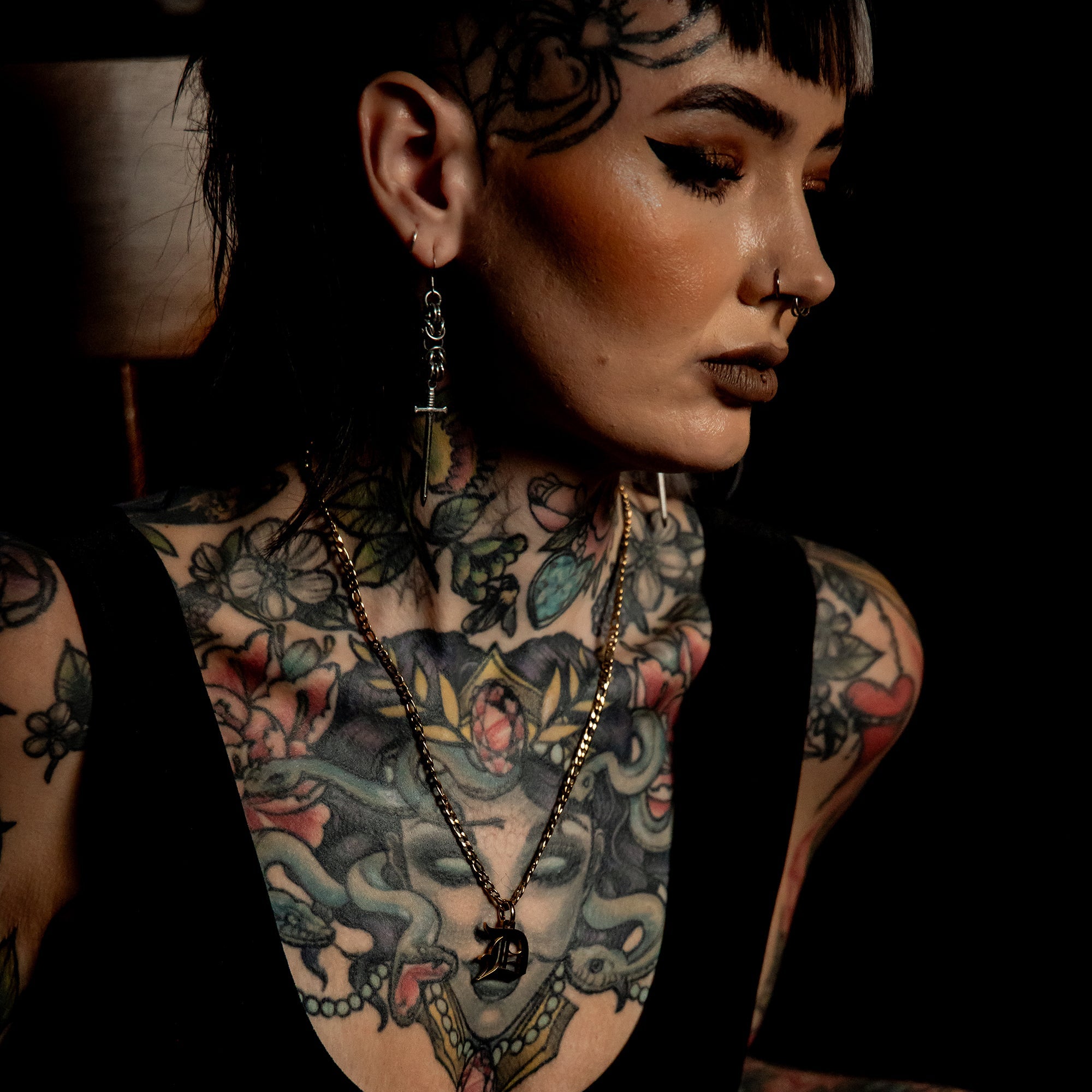 Person with tattoos wearing a black outfit and a Gold Initial cuban necklace