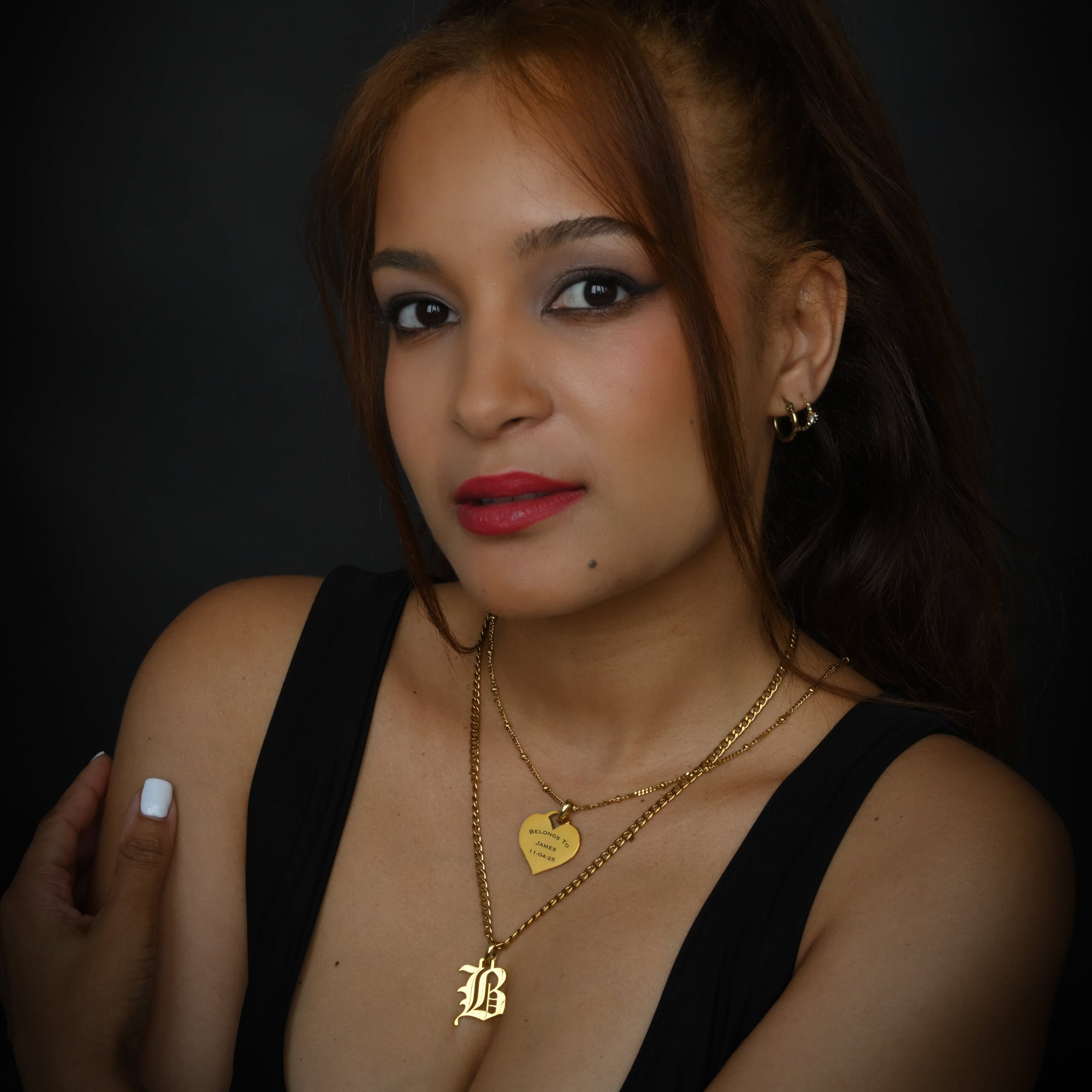 Gold necklace with a heart-shaped engraved pendant and 'B' pendant, worn by a person.