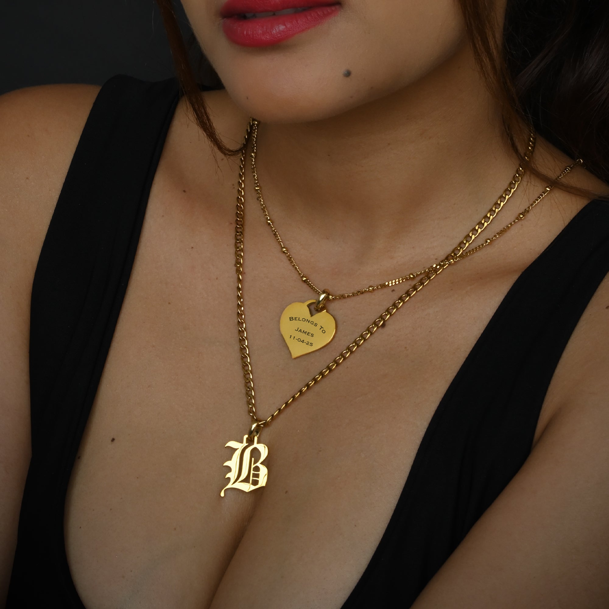 Close-up of a person wearing gold necklaces with visible initial and engraved pendants.