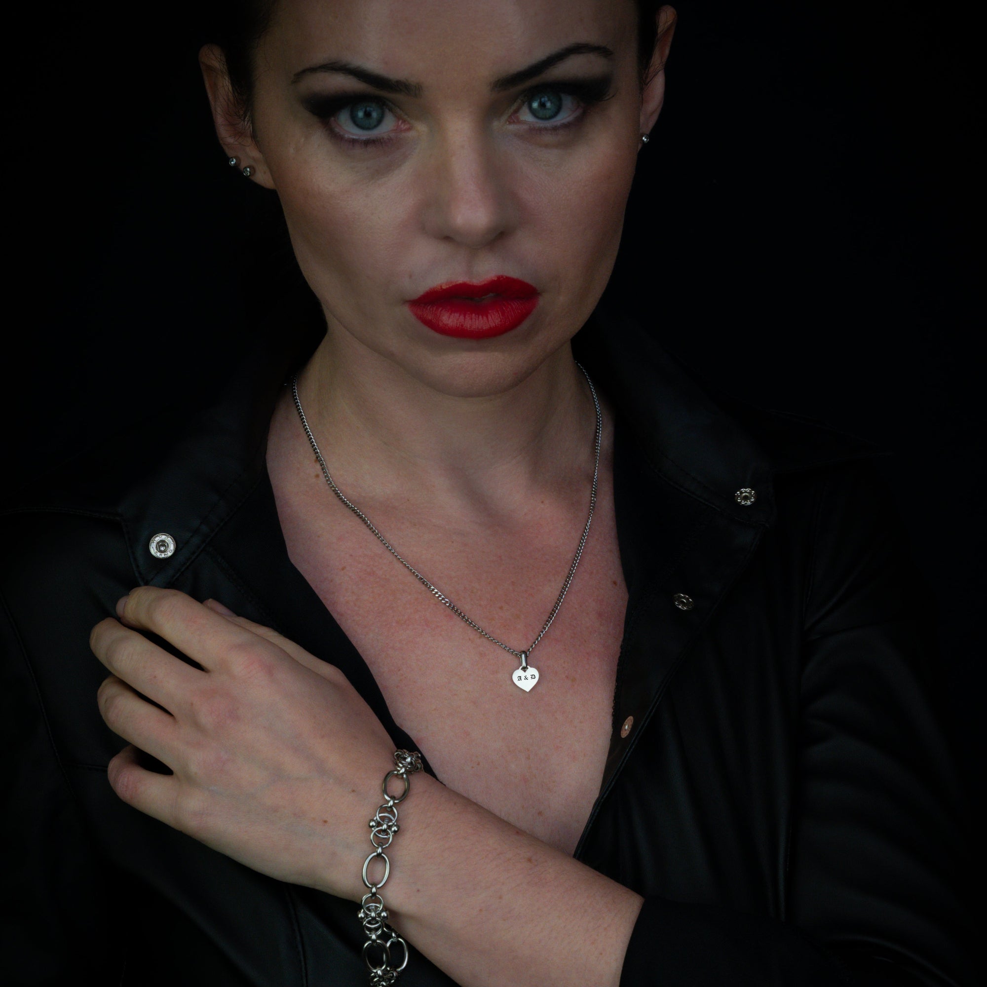 Woman wearing a black outfit with an engraved pendant necklace and bracelet against a dark background