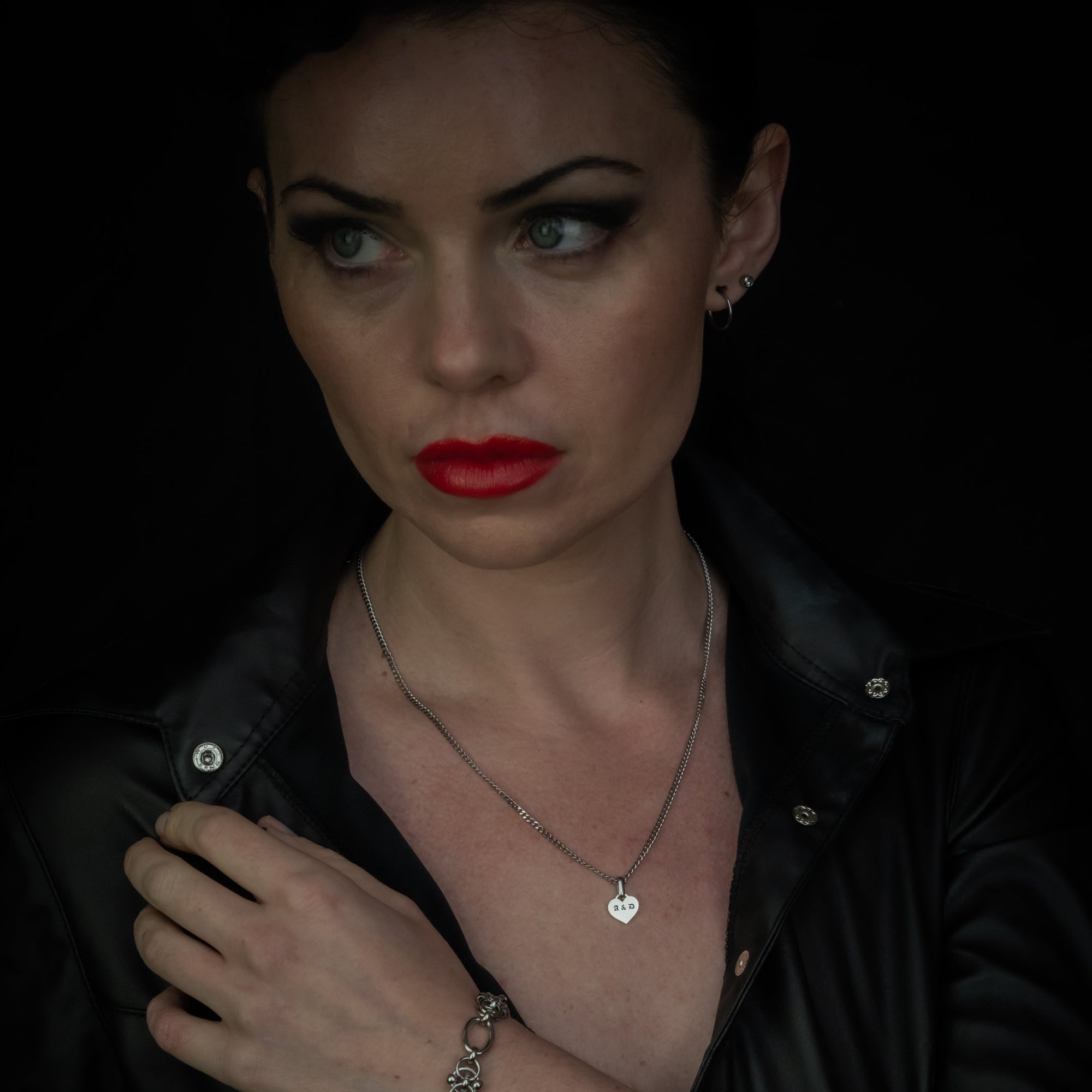 Woman wearing a black outfit with a necklace and bracelet against a dark background