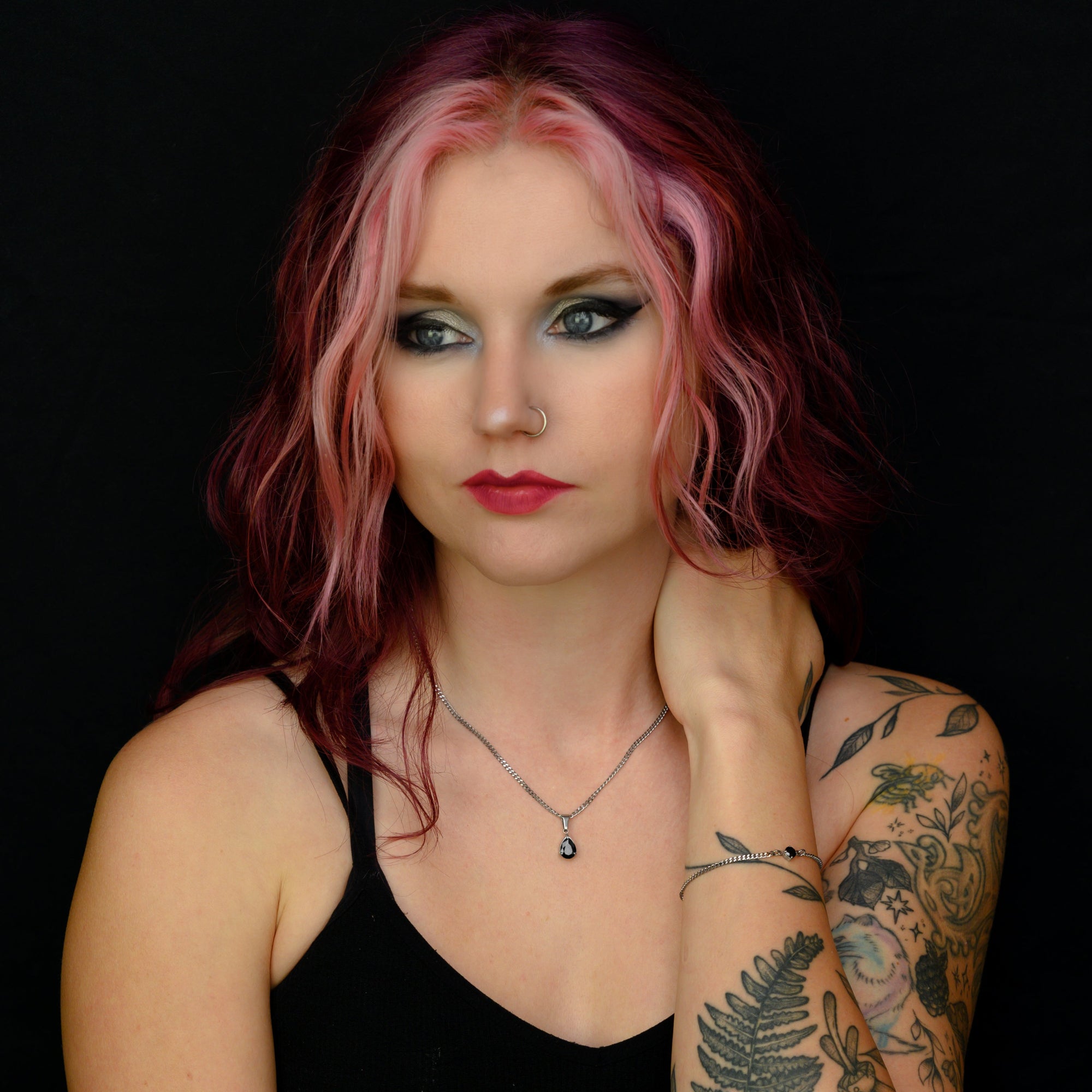 Woman with tattoos and pink hair against a black background wearing a birthstone necklace