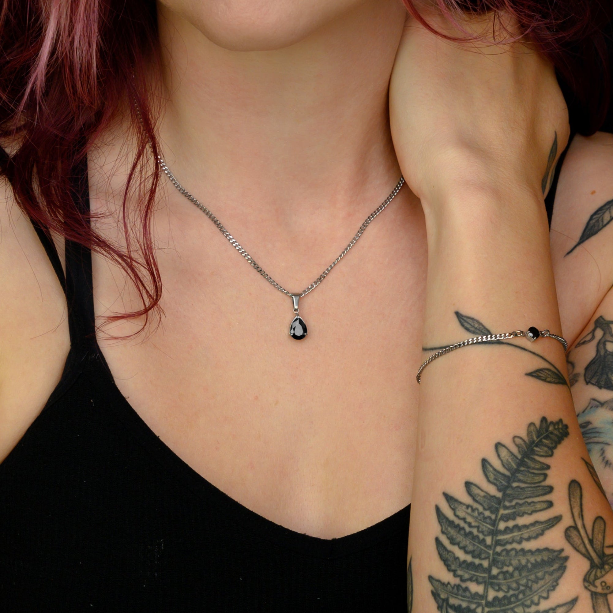 Woman with tattoos and pink hair wearing a black birthstone necklace against a black background