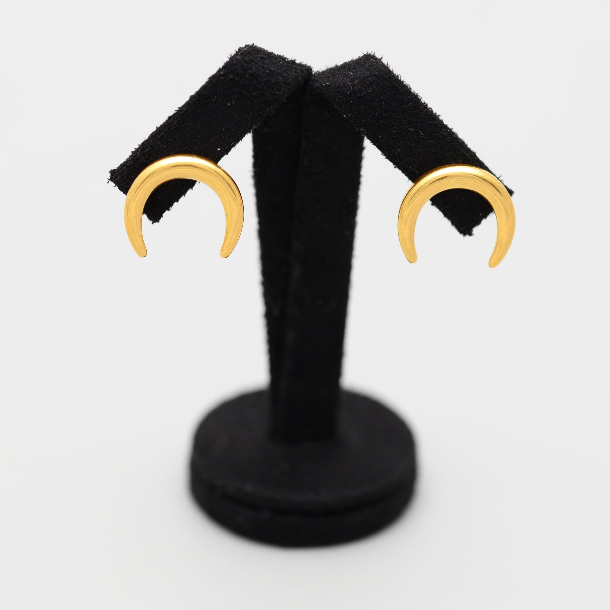 Gold crescent moon earrings on a black stand against a white background