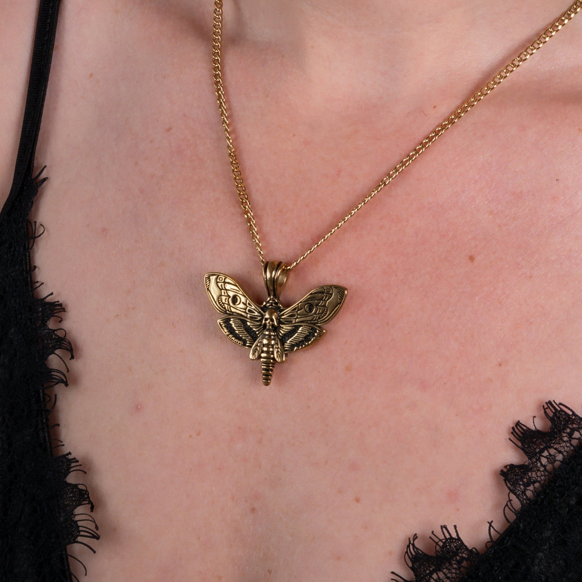 Woman wearing a gold death's head moth pendant on a dainty cuban chain necklace 