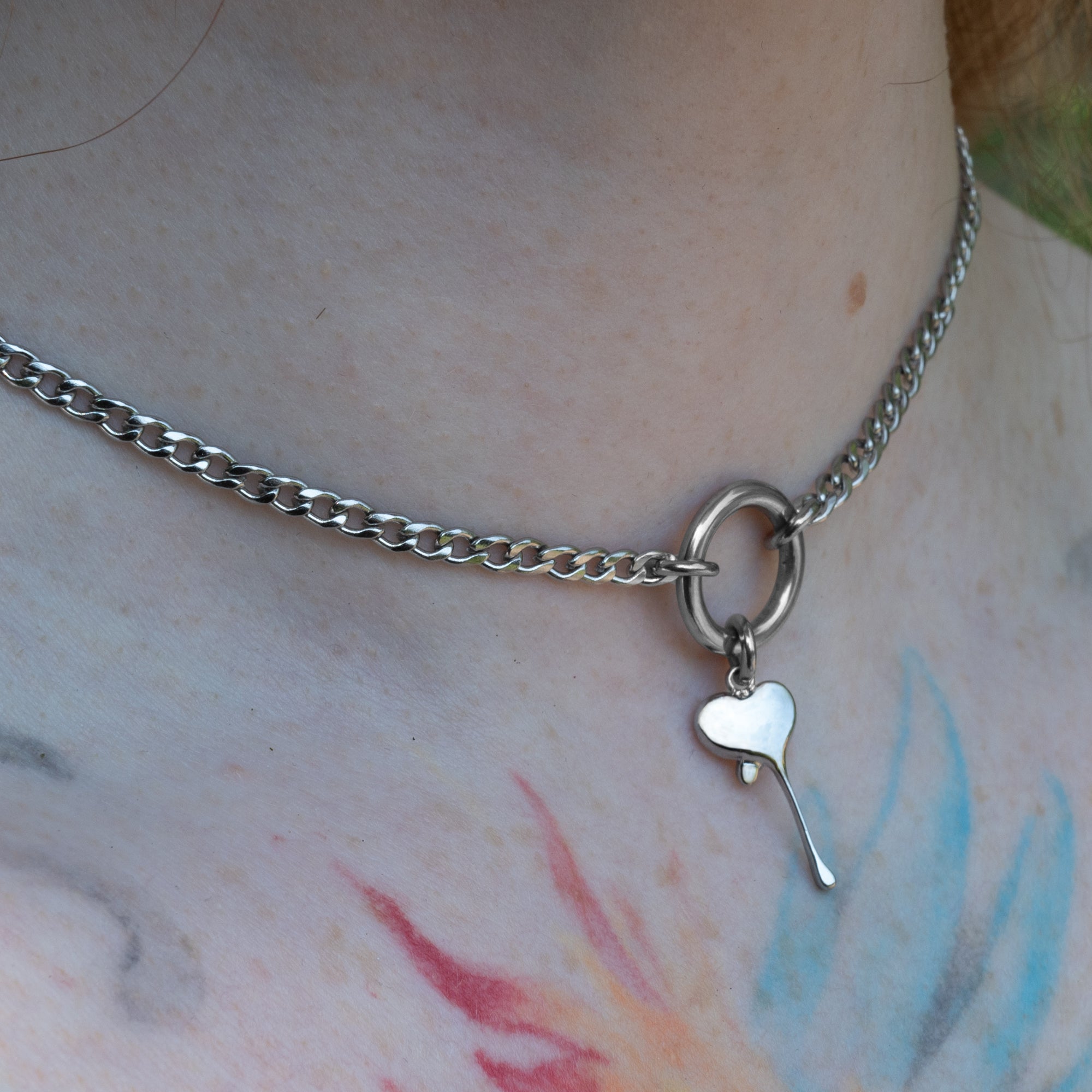 A silver coloured dainty dripping heart pendant on a small O ring day collar 