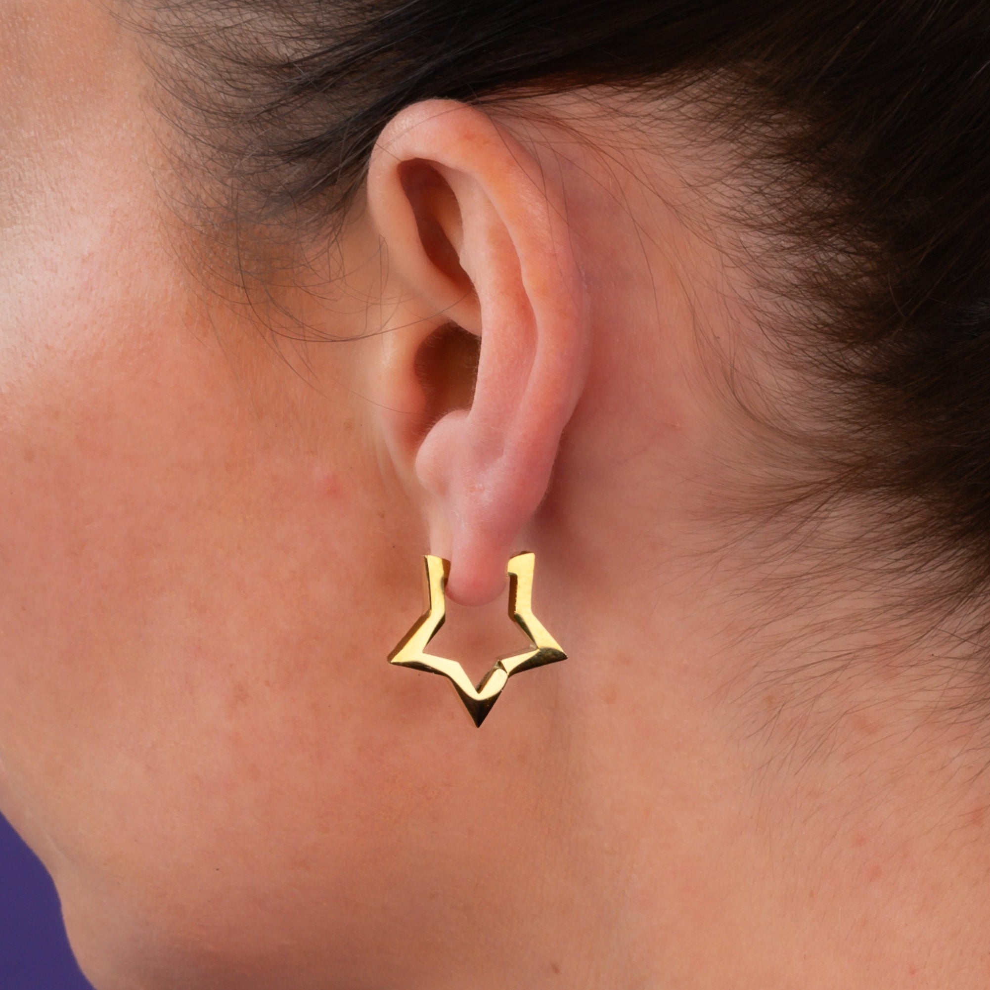 Woman wears gold star huggie earrings with chunky gold cuabn choker