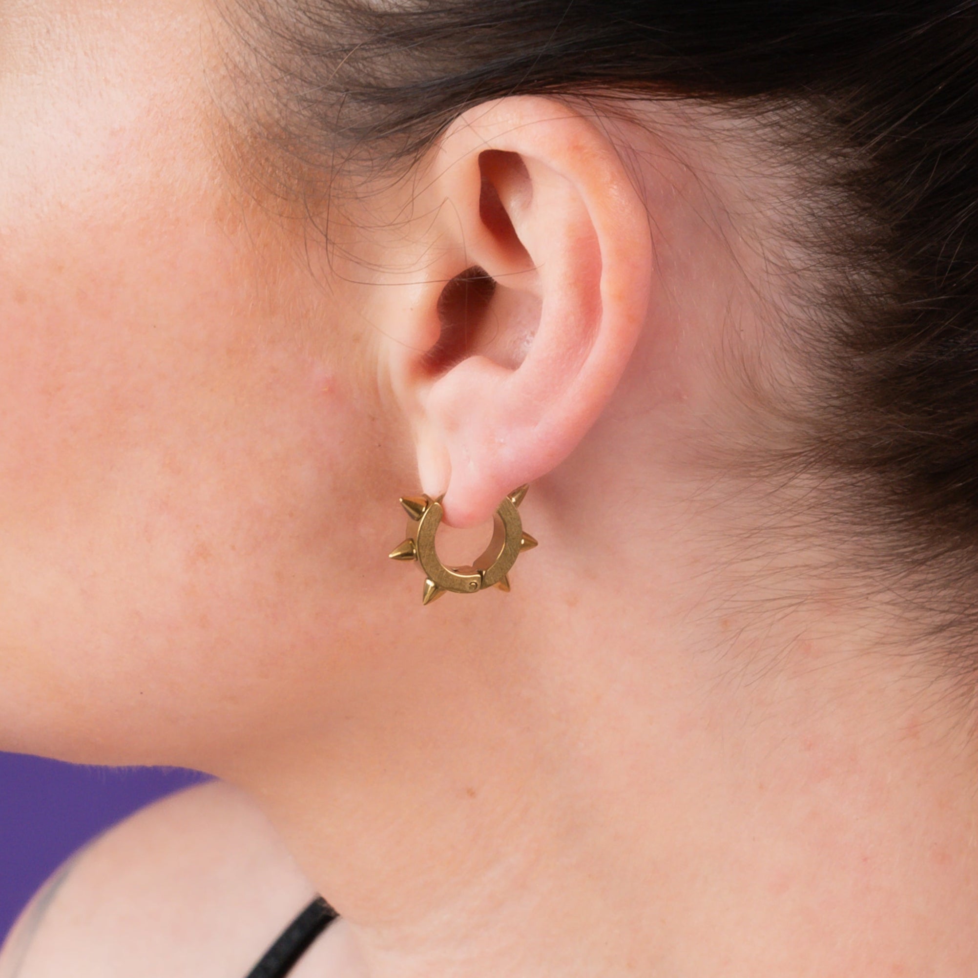 Gold spiky hoop earring worn by a woman 