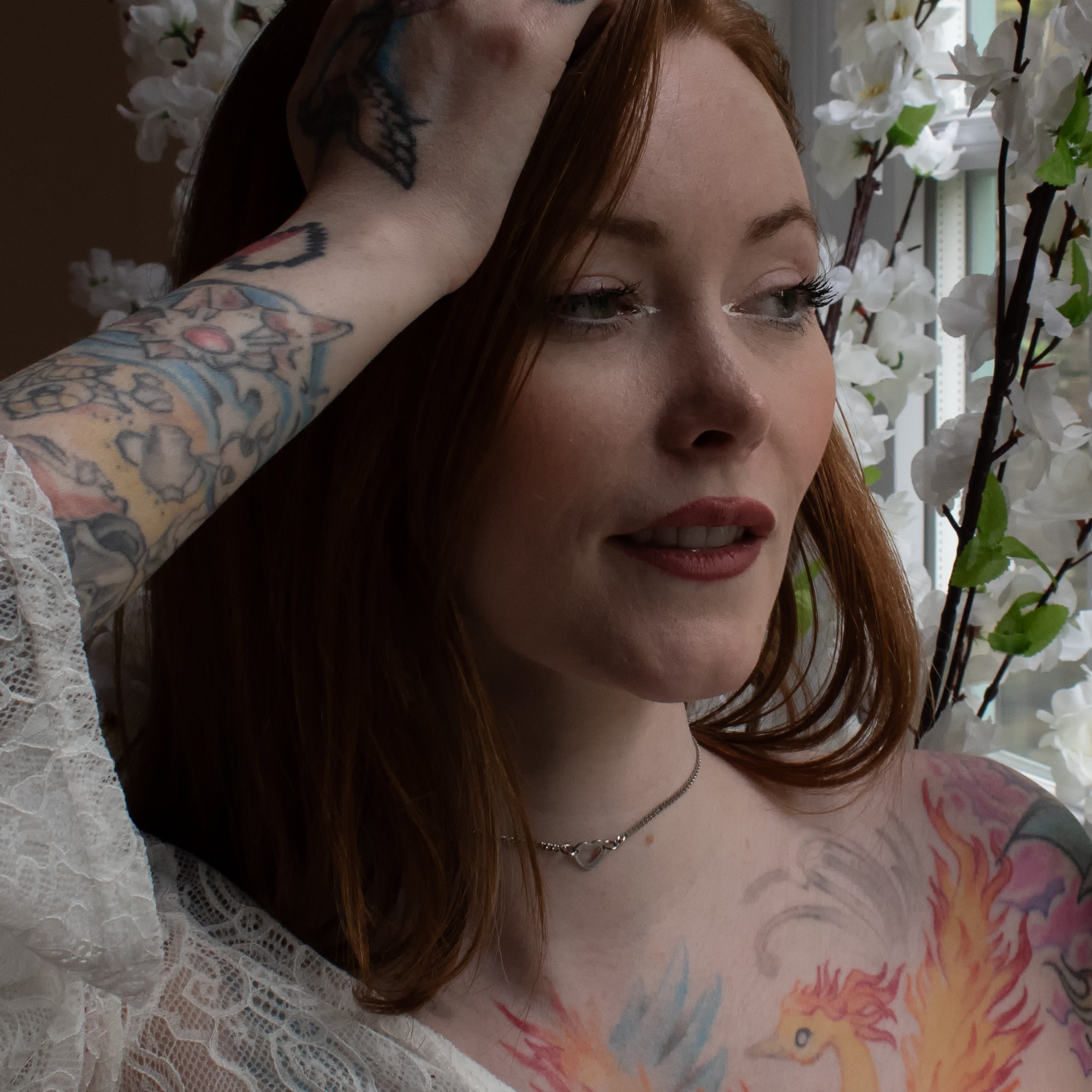 Close up of a dainty heart pendant day collar, silver in colour on a delicate cuban chain, worn by a female model