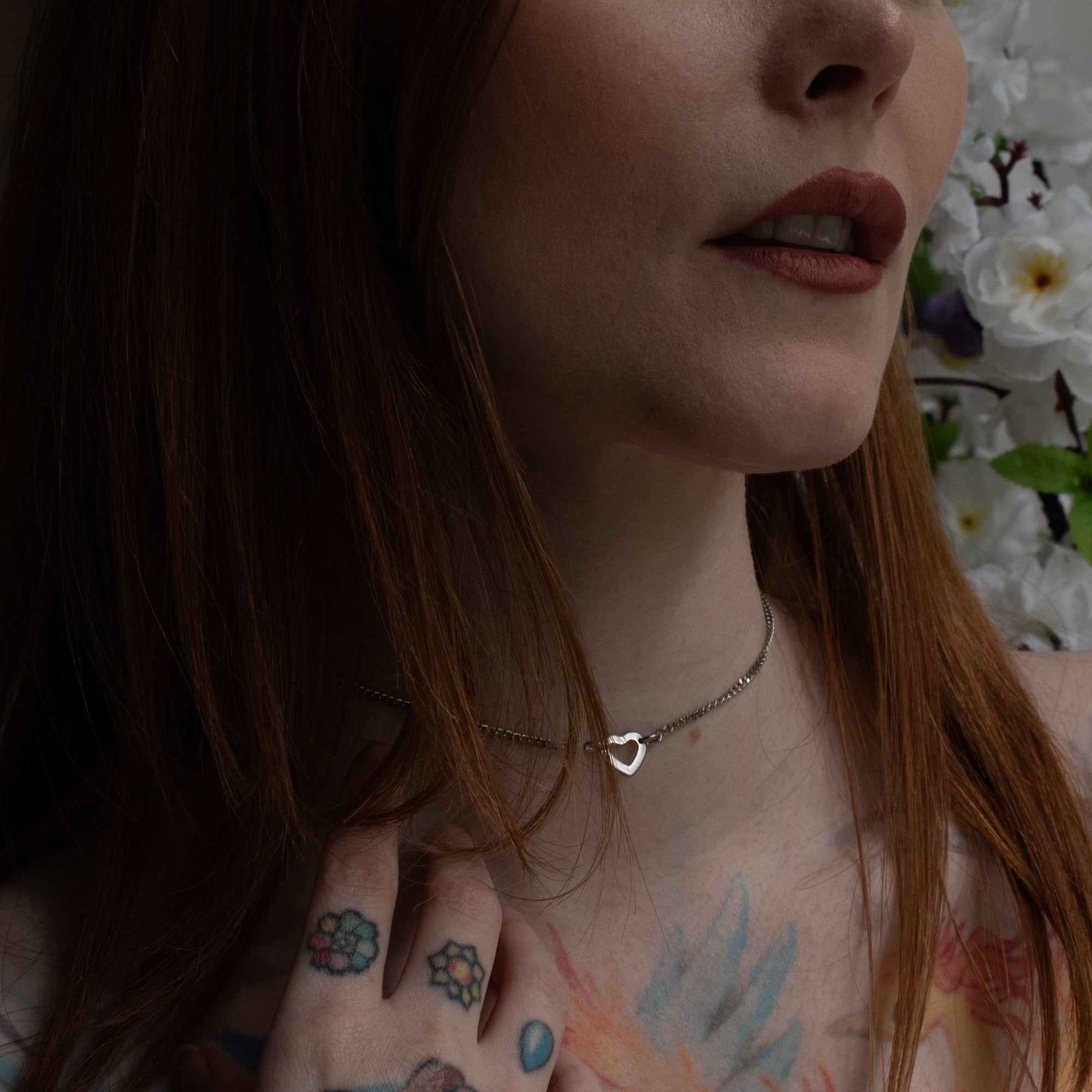 Close up of a dainty heart pendant day collar, silver in colour on a delicate cuban chain, worn by a female model