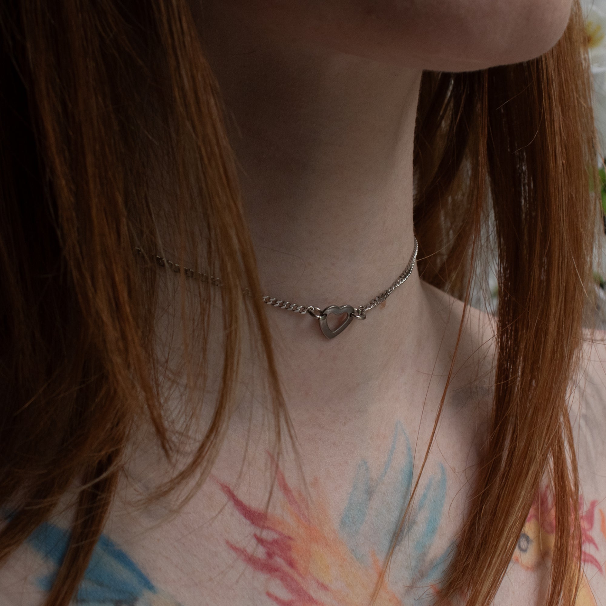 Close up of a dainty heart pendant day collar, silver in colour on a delicate cuban chain, worn by a female model