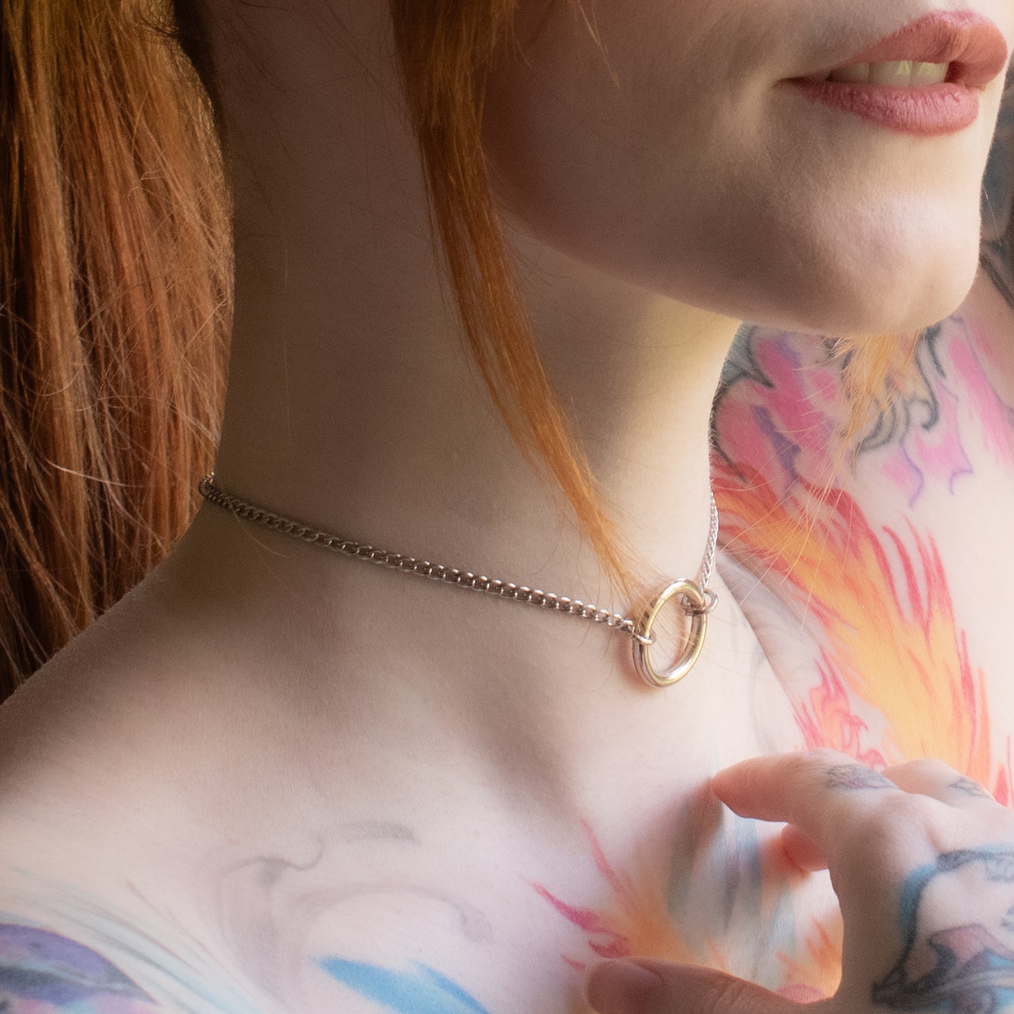 Close up of a small silver coloured O ring day collar on a dainty cuban style chain worn by model