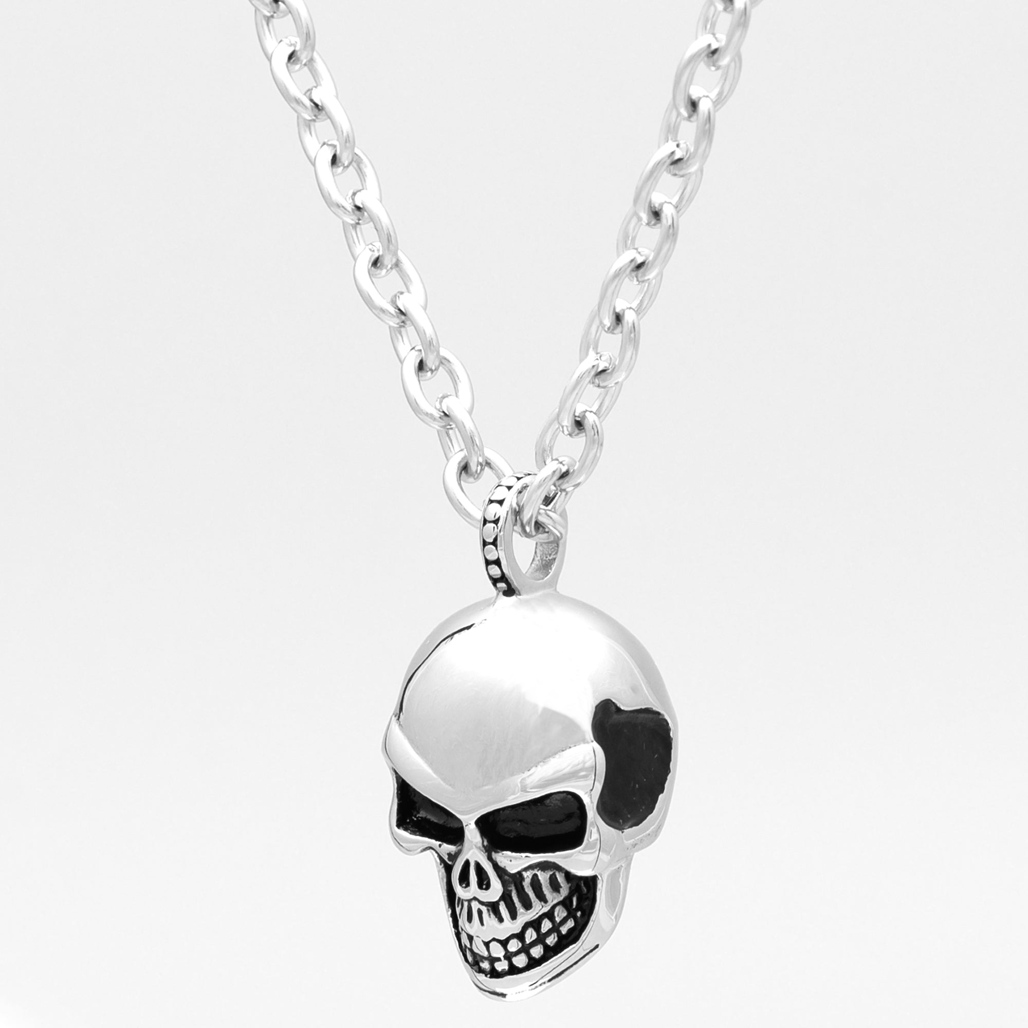 Side view of a large silver anatomical skull pendant on a chunky cable chain necklace