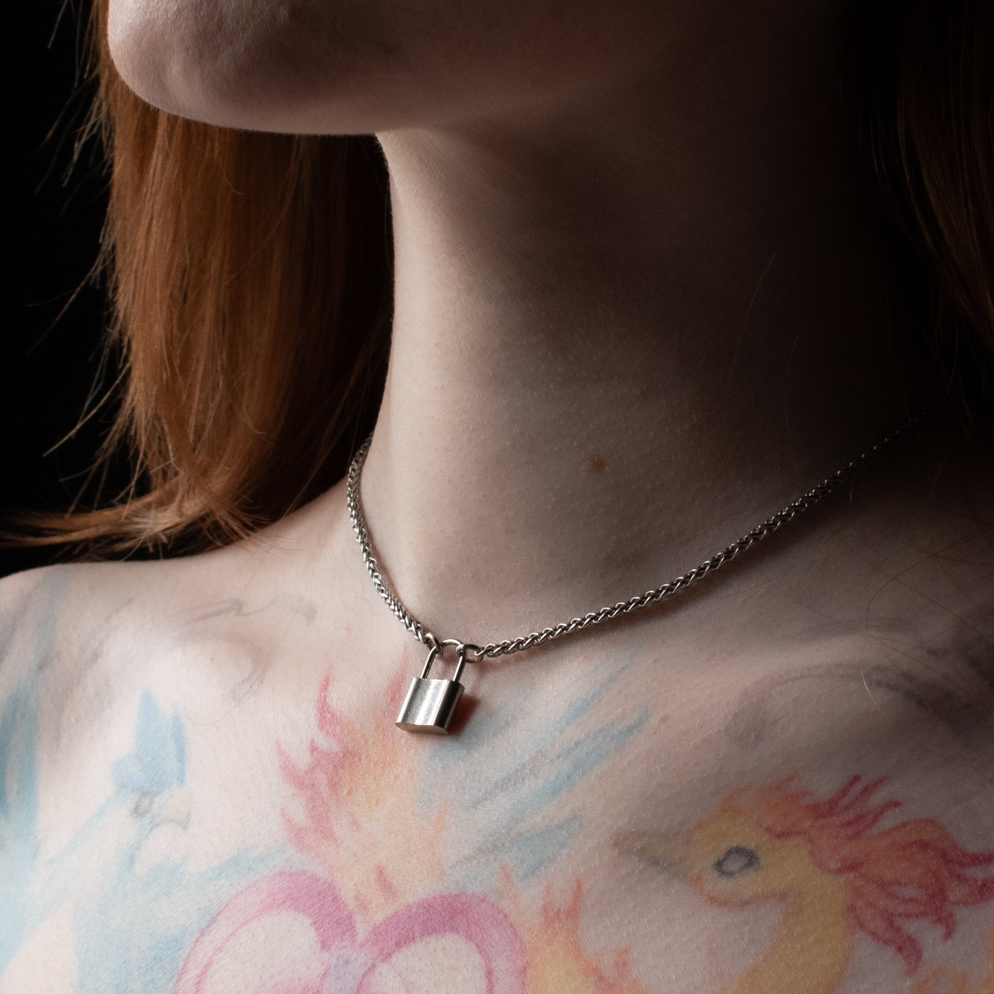 Close up of a silver coloured padlock pendant on a dainty foxtail chain worn by model